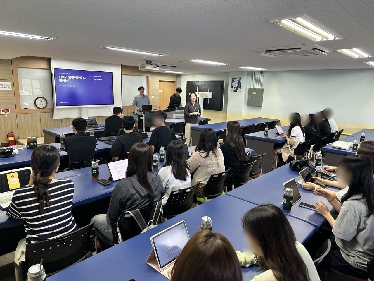 강의실에서 직원들이 각자 노트북과 태블릿으로 실습하며 강사의 설명을 듣는 모습